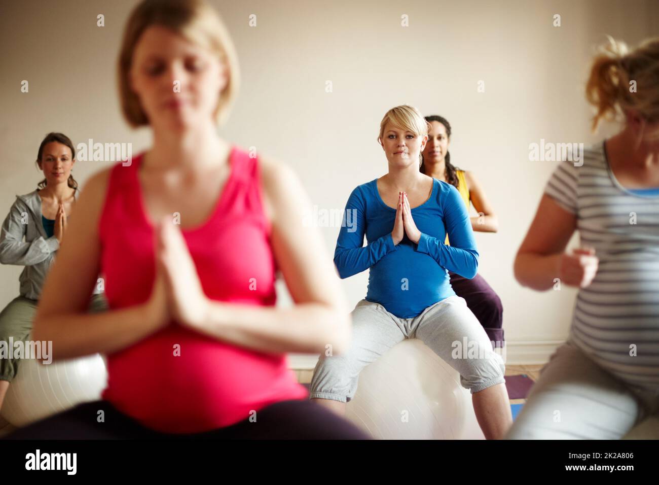 Maternità beata. Un gruppo multietnico di donne incinte che meditano su palle da ginnastica in una classe di yoga. Foto Stock