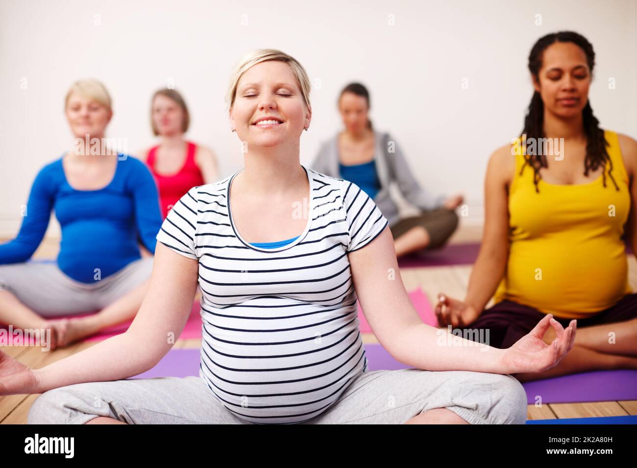 Meditando sulla maternità. Un gruppo multietnico di donne incinte che meditano in una classe di yoga. Foto Stock