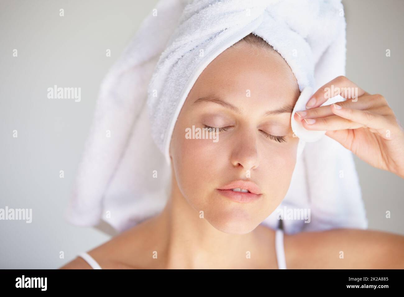 Detergere delicatamente la pelle. Closeup shot di una giovane donna attraente con i suoi capelli avvolti in un asciugamano rimuovere trucco. Foto Stock