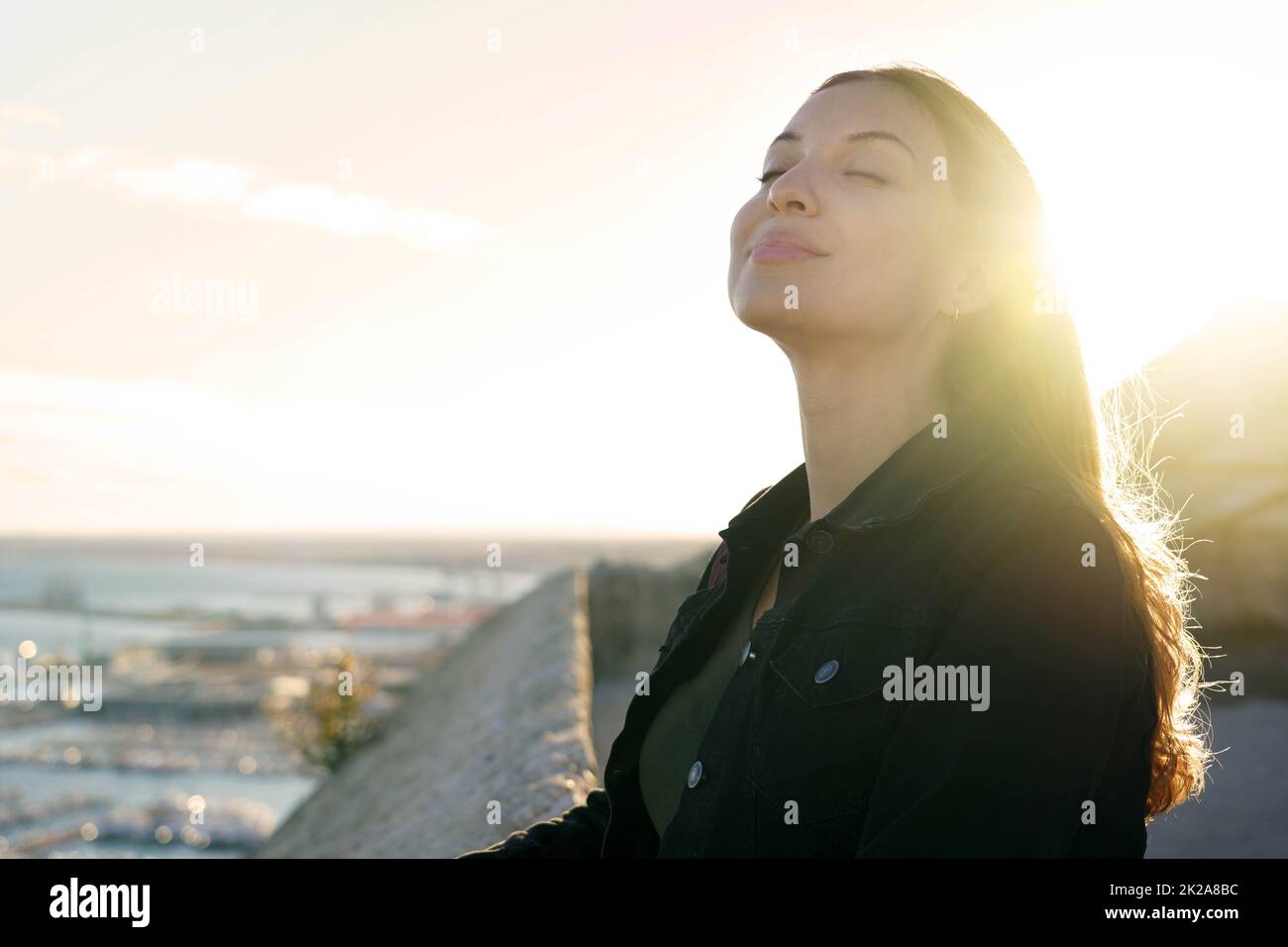 Bella giovane donna con occhi chiusi respirando rilassante godendo il sole al tramonto. Bellezza sole ragazza profilo laterale ritratto. Emozione positiva vita successo mente concetto di pace. Foto Stock