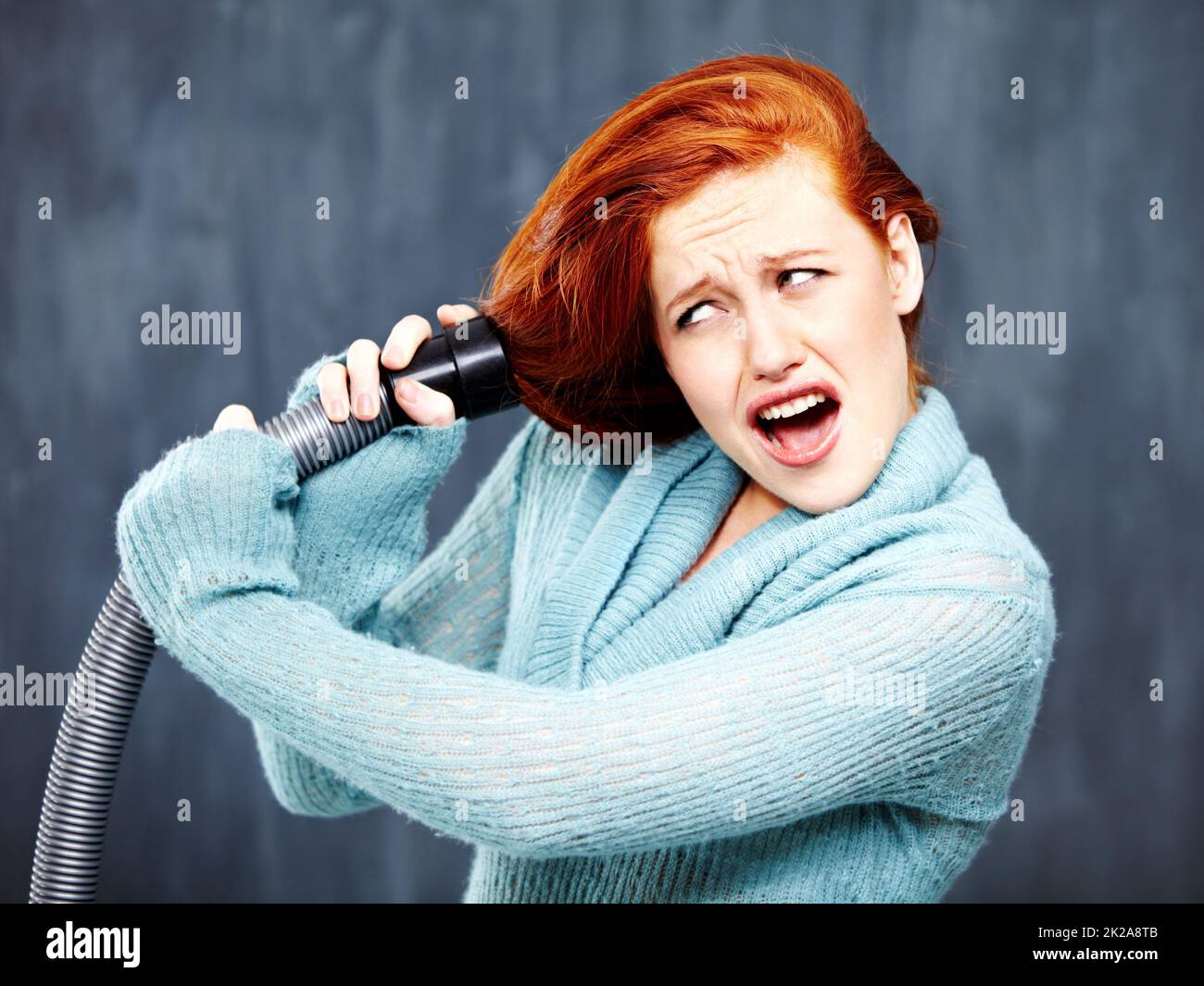 Non è il modo migliore per pulire i capelli. Una giovane redhead con i capelli incastrati nell'aspirapolvere. Foto Stock