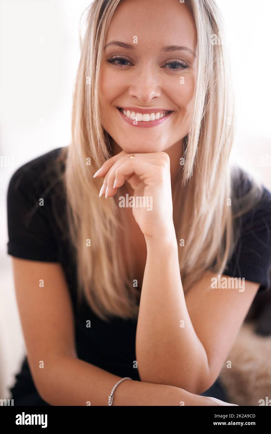 Il suo sorriso mette tutti a proprio agio. Ritratto di una giovane donna seduta con la mano sul mento. Foto Stock