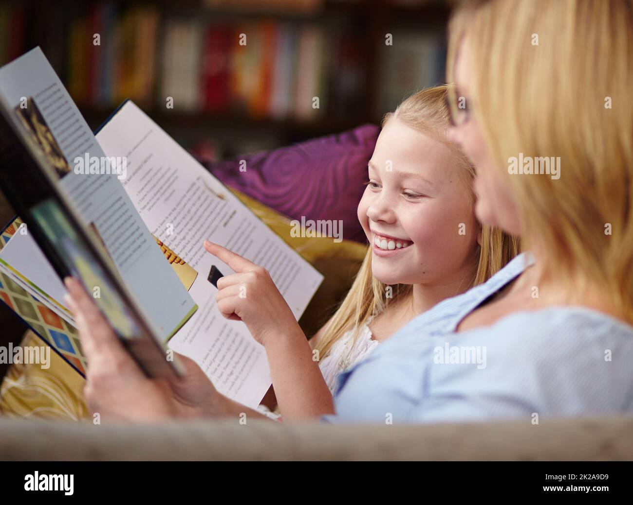 Lettura comune. Una ragazza giovane carina seduta accanto a sua madre mentre leggono un libro. Foto Stock