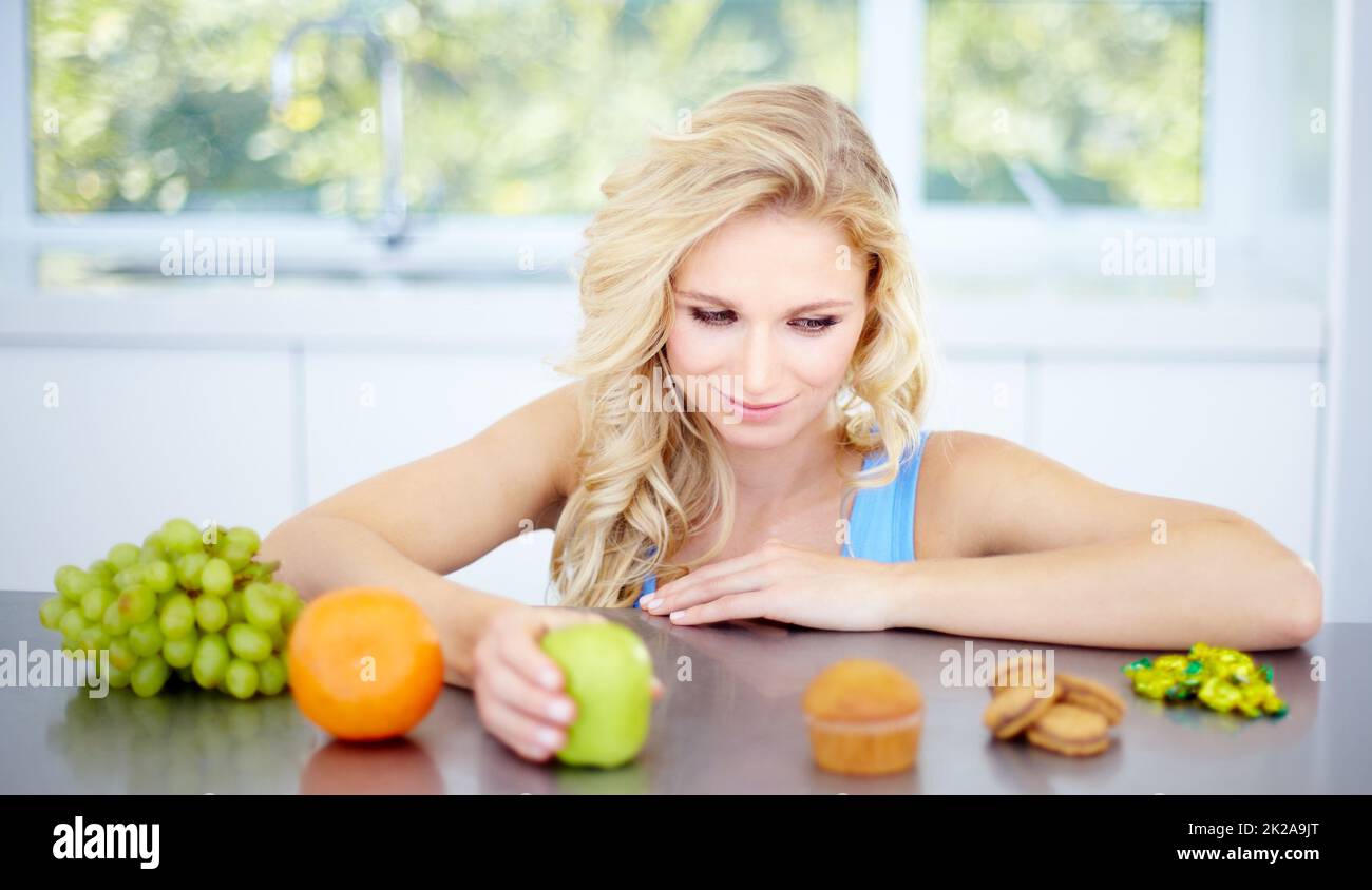 Tentazione - mangiare a destra e rimanere in salute. Donna piuttosto giovane che è tentata di mangiare cibo malsano. Foto Stock