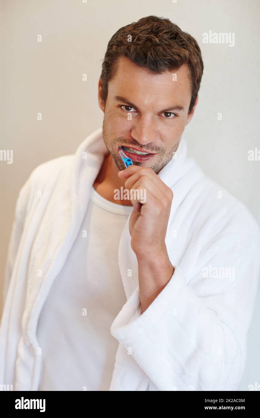 Igiene dentale. Un bell'uomo in un accappatoio sorridendo alla fotocamera mentre tiene uno spazzolino. Foto Stock