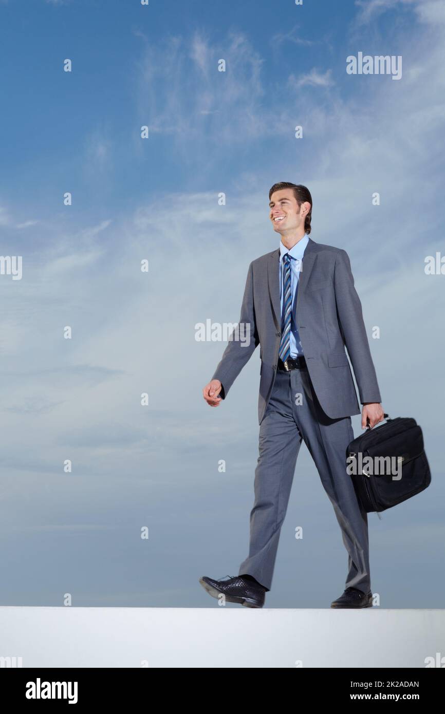 Passeggiando verso il successo. Un giovane uomo d'affari che porta la sua valigetta contro un cielo blu. Foto Stock