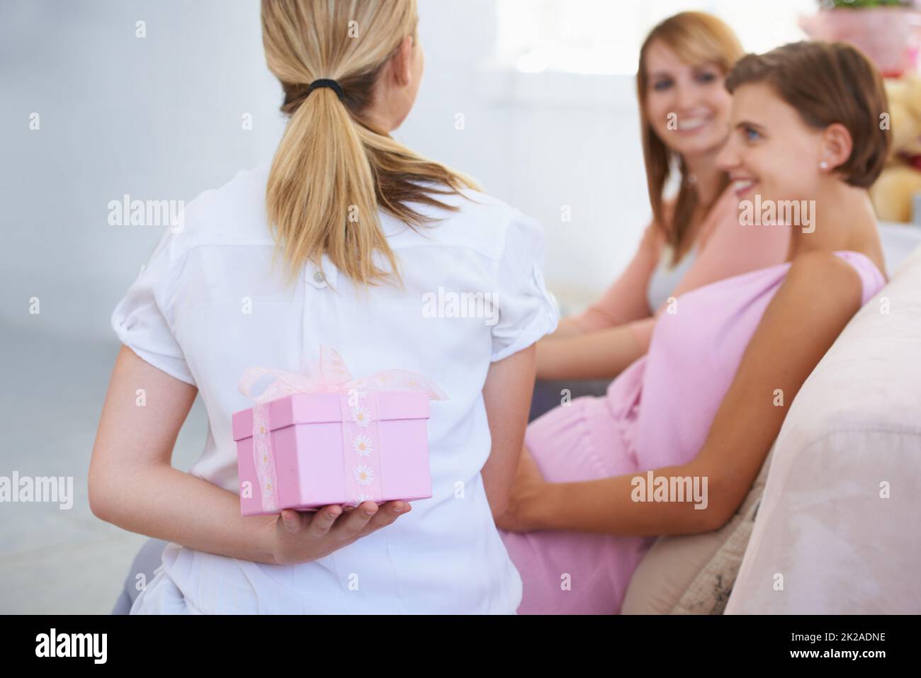 Prolungamento dell'attesa. Una giovane donna che nasconde un regalo dietro la schiena ai suoi amici babyshower. Foto Stock