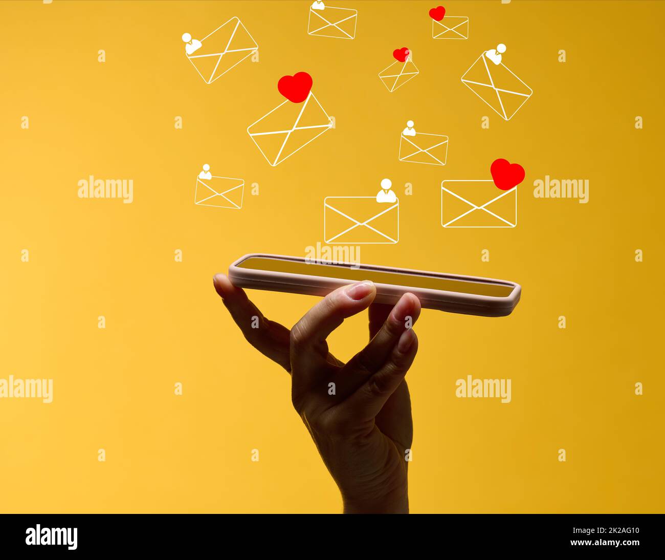 la mano femminile tiene uno smartphone con lettere volanti su sfondo giallo. Dipendenza dai social media, ricezione di corrispondenza e valutazione. Foto Stock