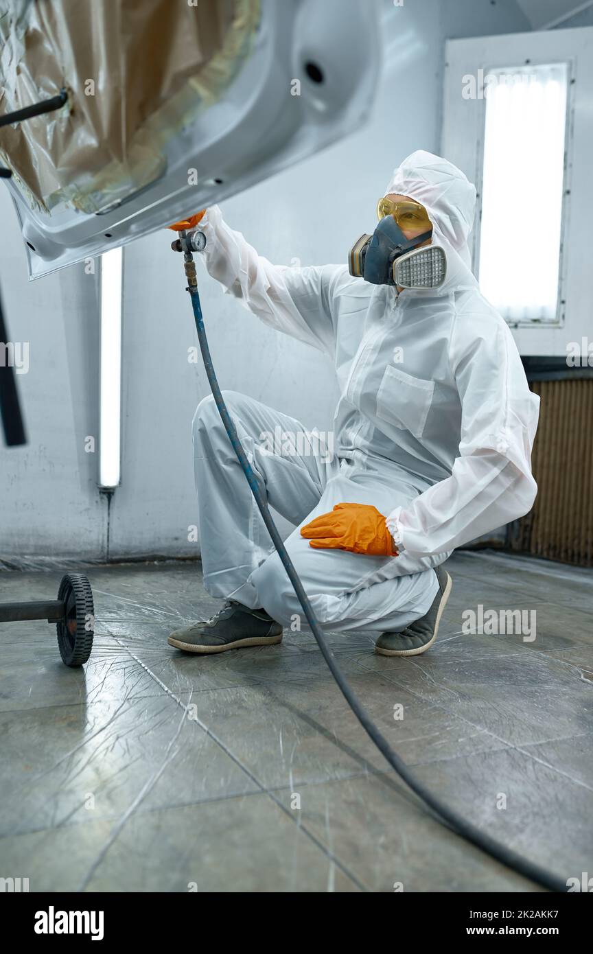 Tecnico in abbigliamento di sicurezza spruzzando vernice per auto Foto Stock