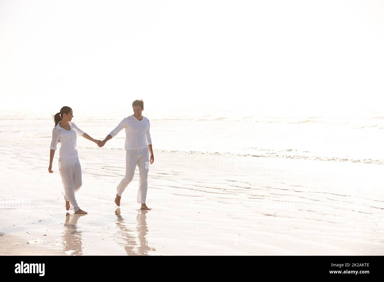 Tenere le mani attraverso la bellezza della natura. Scatto a tutta lunghezza di una giovane coppia attraente vestita di bianco camminando lungo una spiaggia. Foto Stock