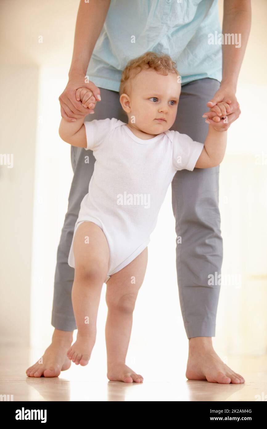 Prendendo i suoi primi passi.... Immagine ritagliata delle gambe di un bambino che cammina con un genitore che sostiene da dietro. Foto Stock
