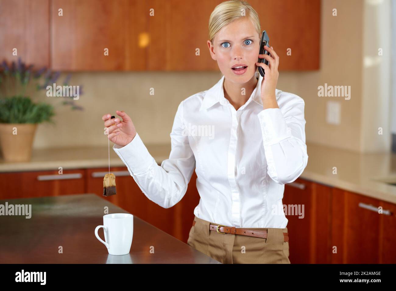 Incredulità. Una bella giovane donna che riceve una chiamata stupefacente mentre fa il tè. Foto Stock