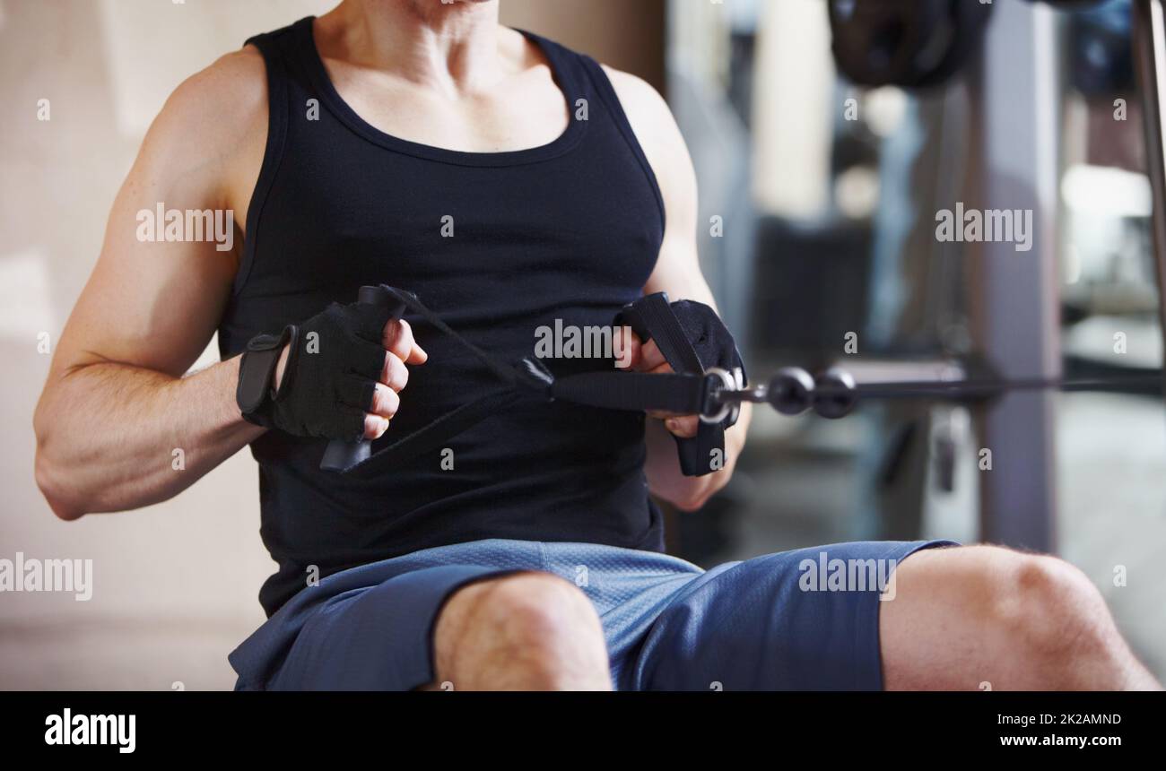 Rafforzando il suo nucleo. Immagine ritagliata di un uomo maturo che utilizza la macchina della fila di cavi in palestra. Foto Stock