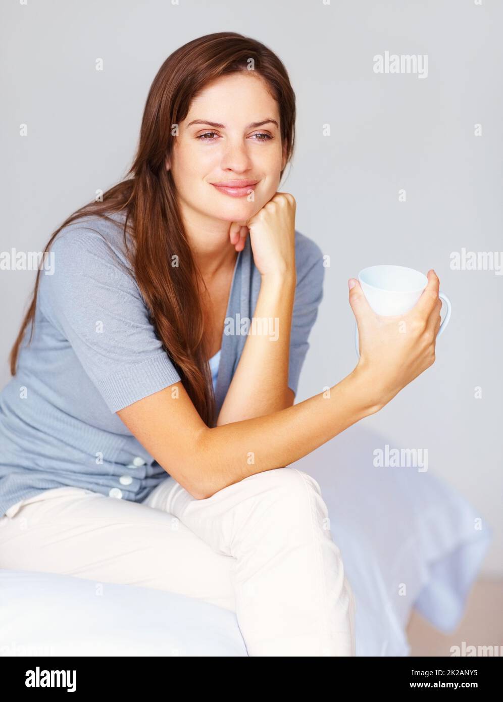 Donna premurosa che beve una tazza di caffè in camera da letto. Day Dreaming - Pretty femmina informale bere caffè e sedersi rilassato sul letto. Foto Stock