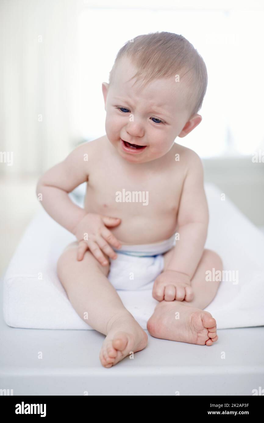 Turbato da un mal di pancia. Un bambino che piange seduto su un tavolo cambiante. Foto Stock