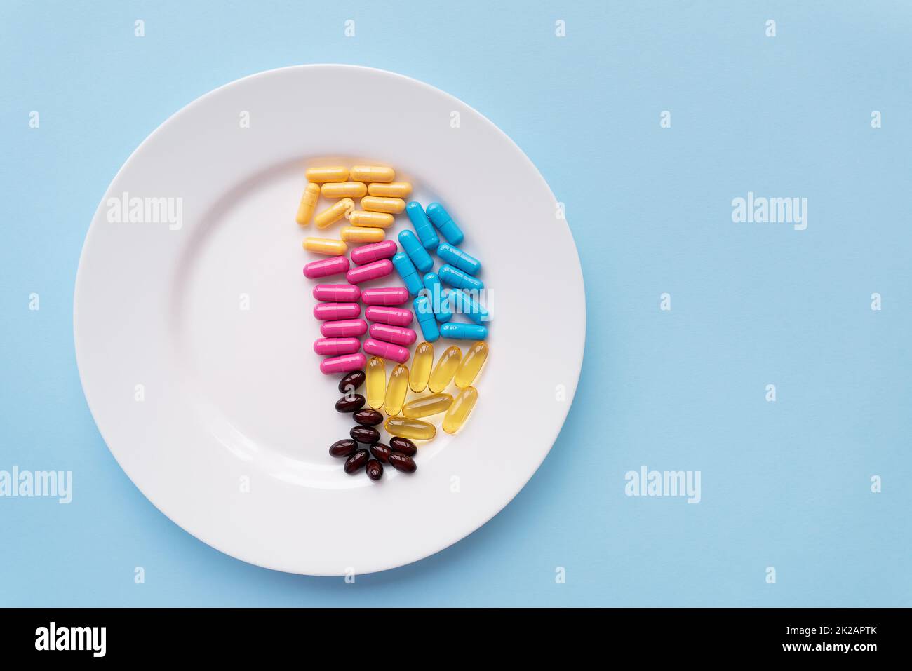 Piatto bianco con pillole di integratori alimentari in diversi colori luminosi. Sfondo blu, posto per un'iscrizione. Foto Stock