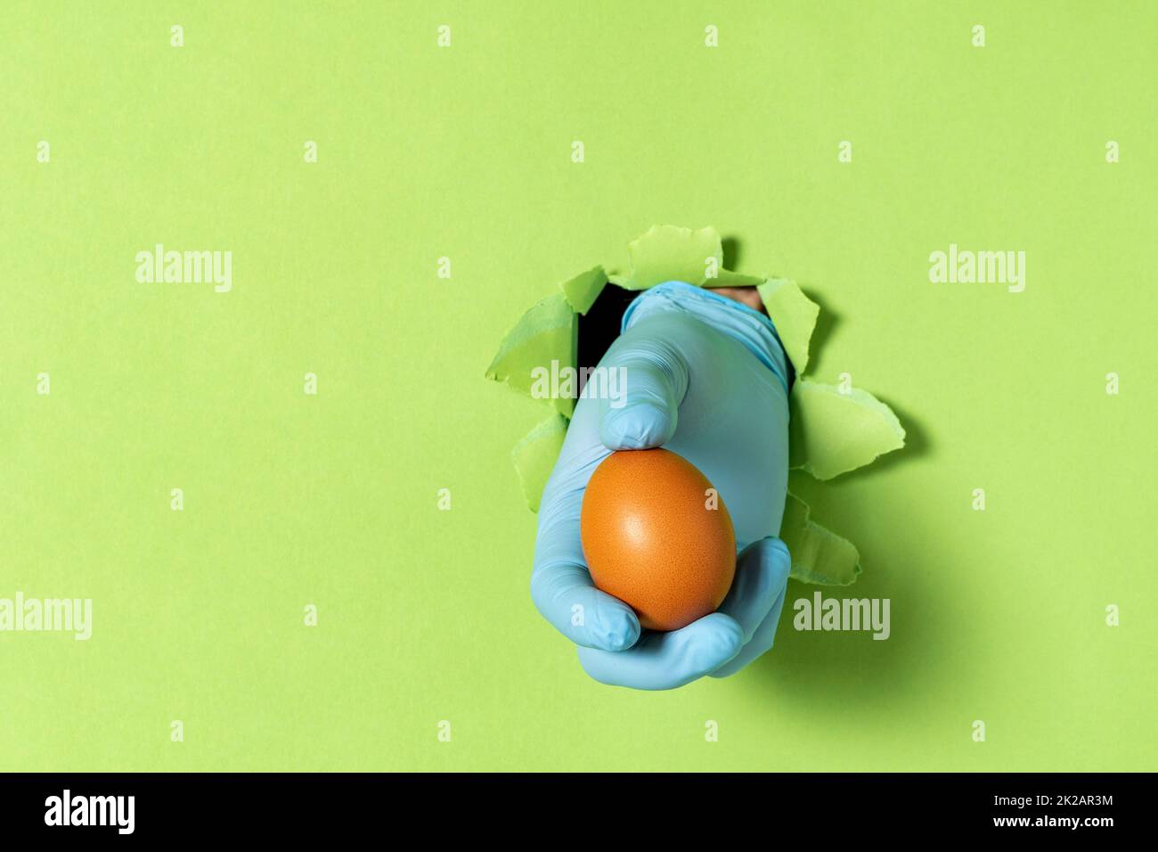 Un uomo tiene in mano un uovo di pollo dopo essersi spezzato su un muro di carta verde Foto Stock