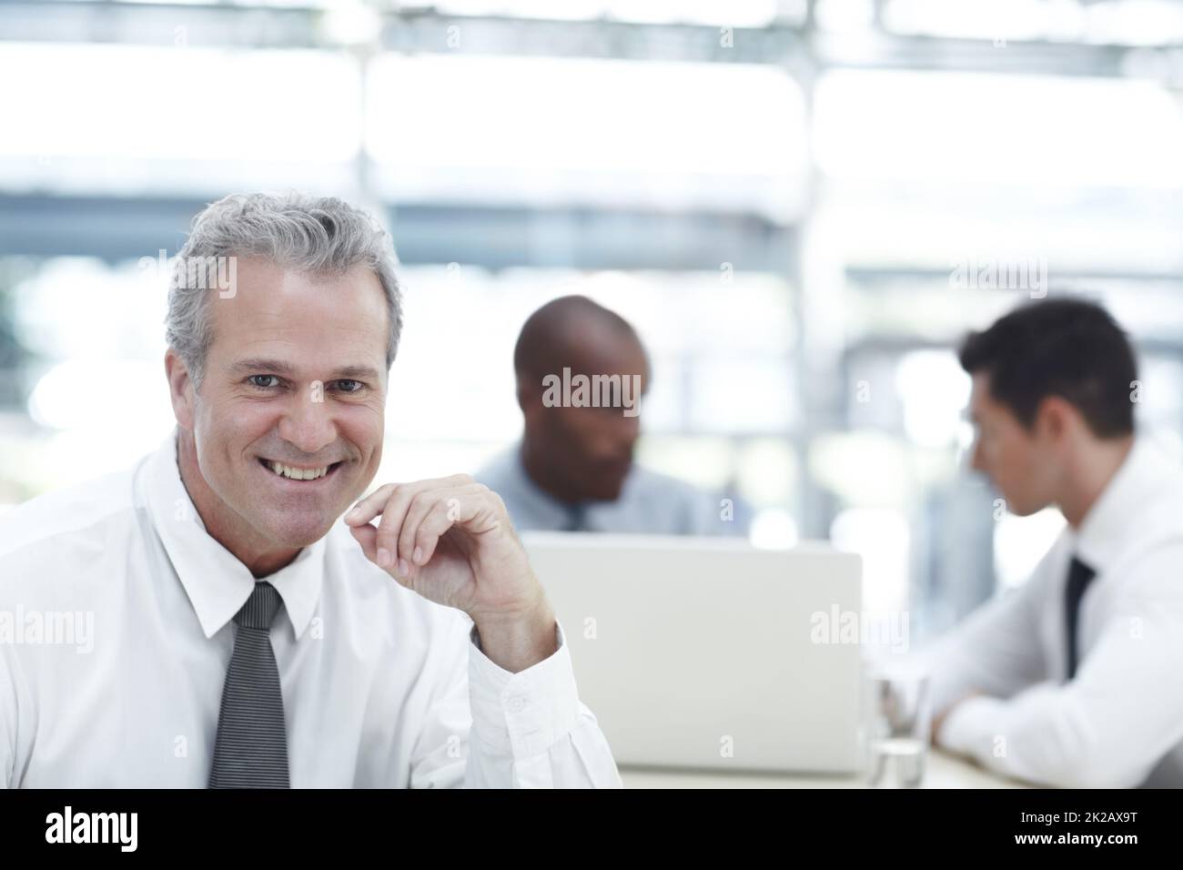 HES un datore di lavoro ben equilibrato. Ritratto di un uomo d'affari maturo sorridente mentre si siede di fronte a due colleghi più giovani. Foto Stock