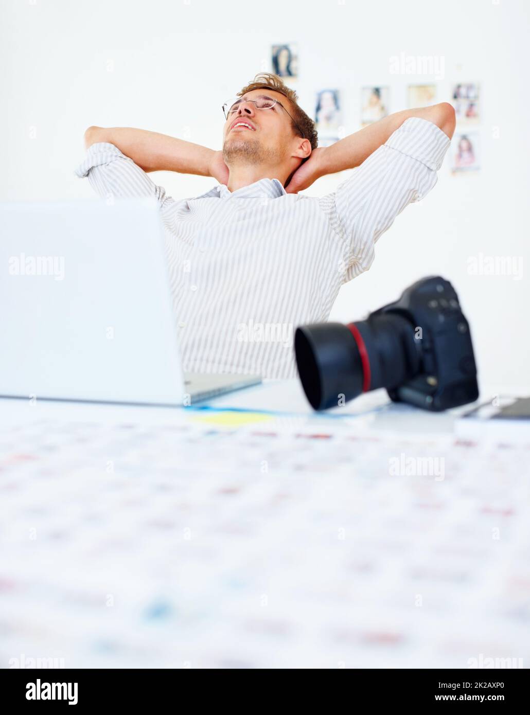 Fotografo rilassante. Fotografo che utilizza un computer portatile e si rilassa con le mani dietro la testa. Foto Stock