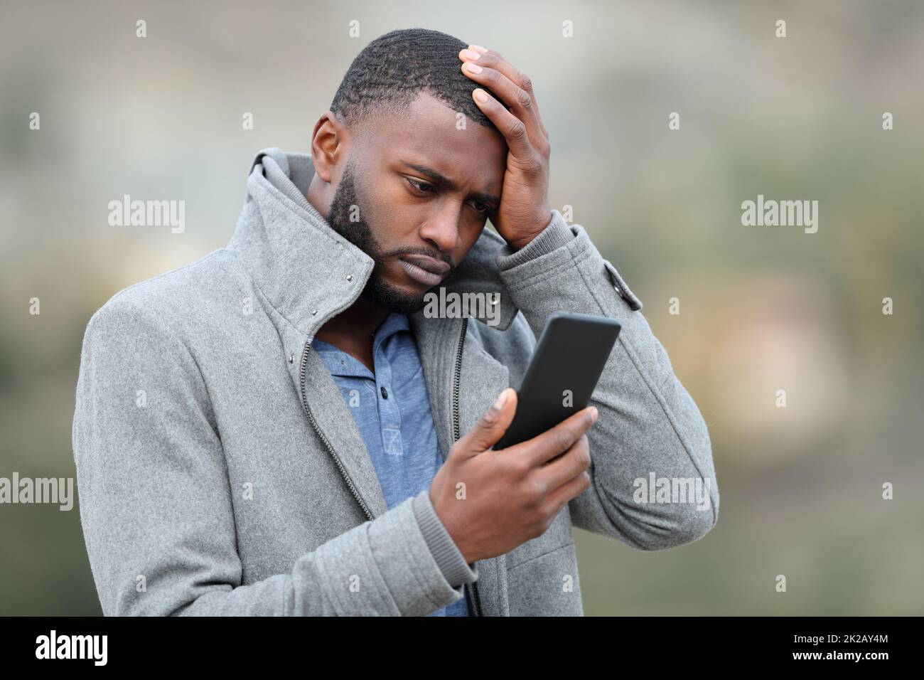 Uomo preoccupato con la pelle nera che controlla il telefono in inverno Foto Stock