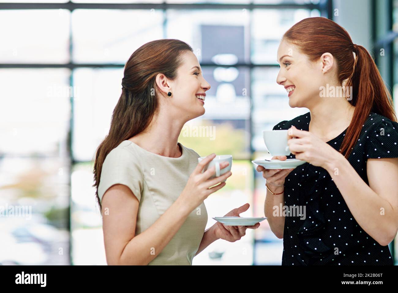 Raccontami tutto sul tuo fine settimana. Scatto corto di due donne d'affari in piedi e chiacchierando durante una pausa caffè. Foto Stock