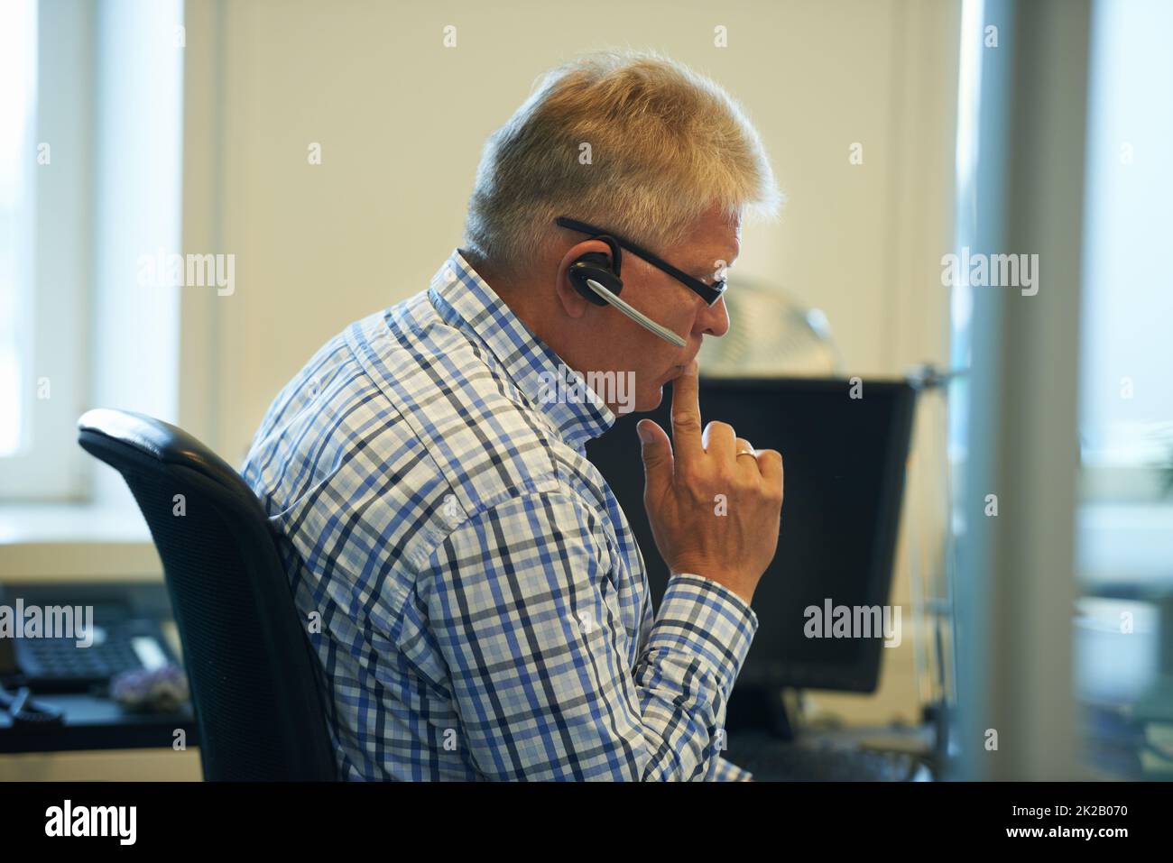La comunicazione è sempre stata la sua forza. Scatto di un uomo d'affari anziano che indossa una cuffia che guarda pensieroso mentre si siede al suo computer. Foto Stock