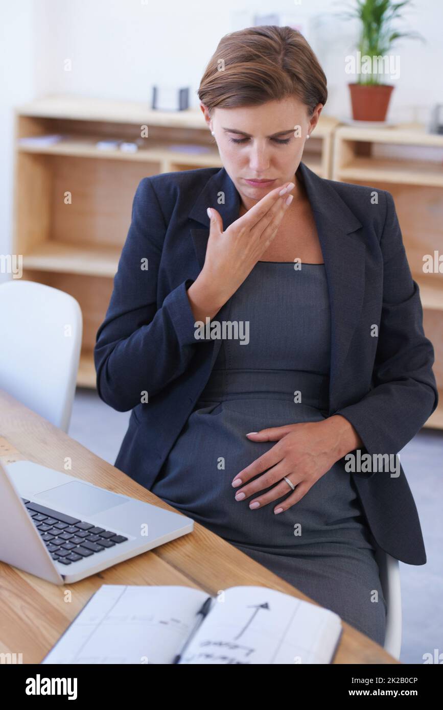 Lotta attraverso la nausea. Una donna d'affari incinta che combatte con nausea alla sua scrivania. Foto Stock