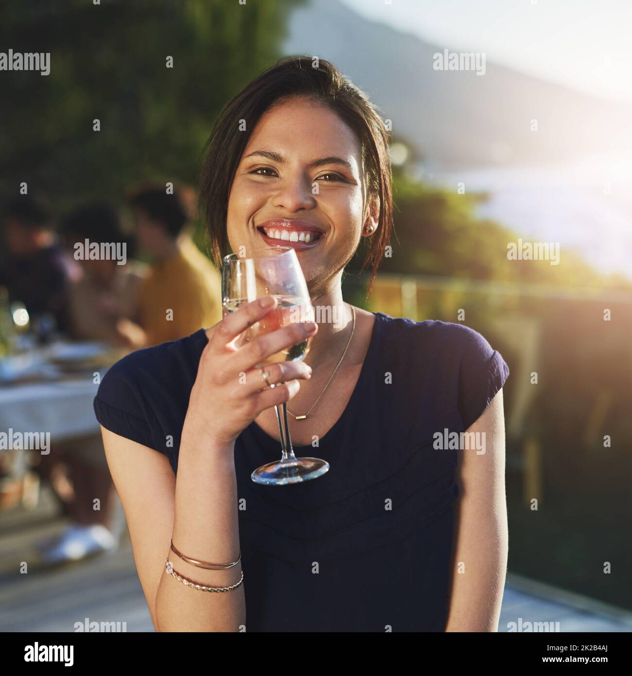 La shes fine come il vino fresco che beve. Scatto di una giovane donna attraente godendo un bicchiere di vino all'aperto con i suoi amici in background. Foto Stock