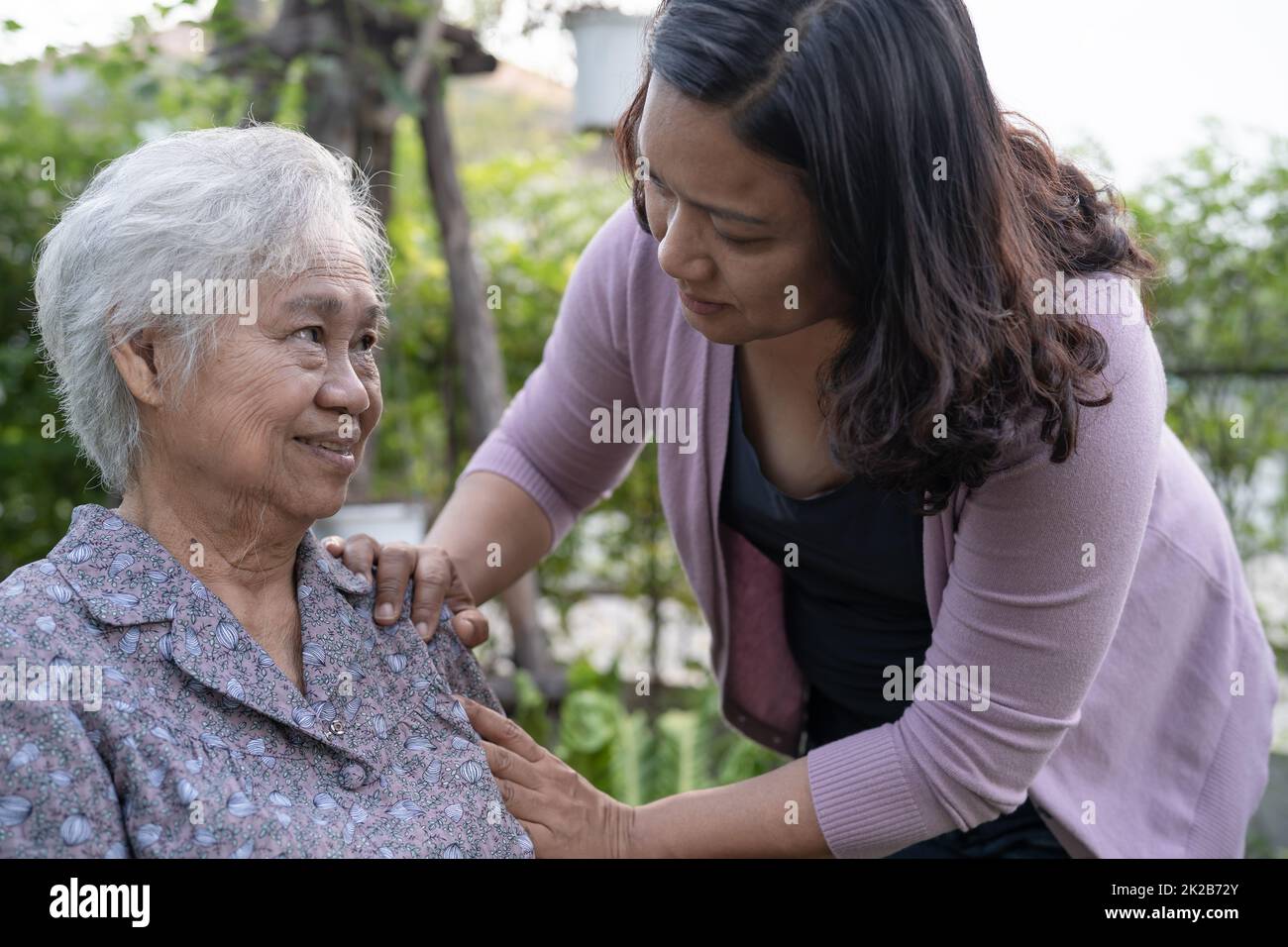 La figlia del caregiver aiuta la donna anziana anziana o anziana asiatica su sedia a rotelle elettrica nel parco. Foto Stock