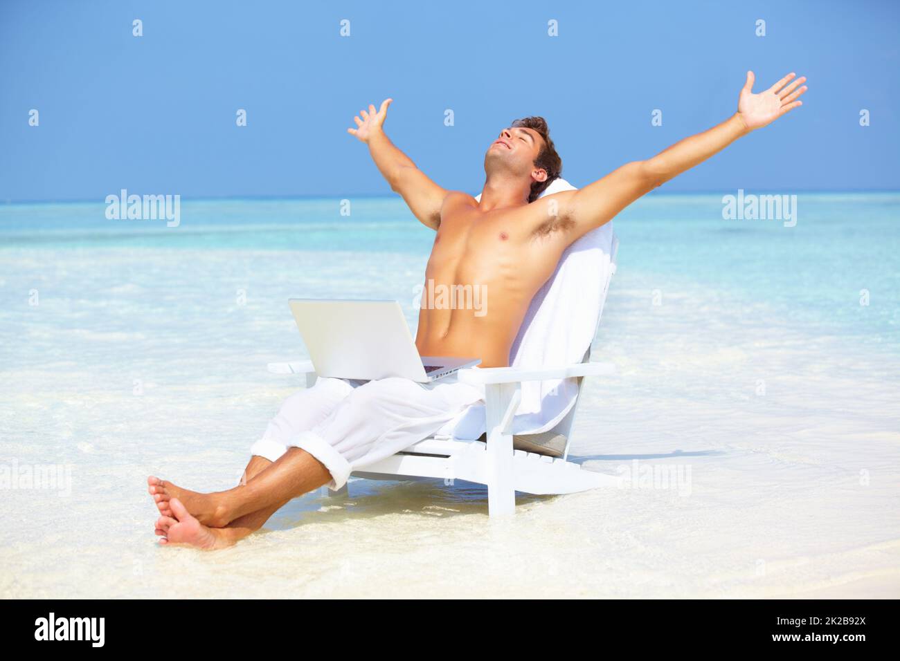 Uomo tranquillo con computer portatile sulla spiaggia. Ritratto di uomo tranquillo stendendo braccia con computer portatile sulla spiaggia. Foto Stock