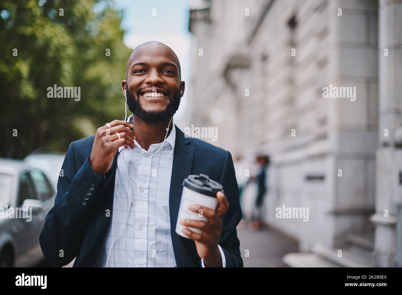 Questa pausa caffè mi ha ispirato di nuovo. Immagine di un uomo d'affari che tiene un caffè e ascolta la musica attraverso gli auricolari mentre cammina per la città. Foto Stock