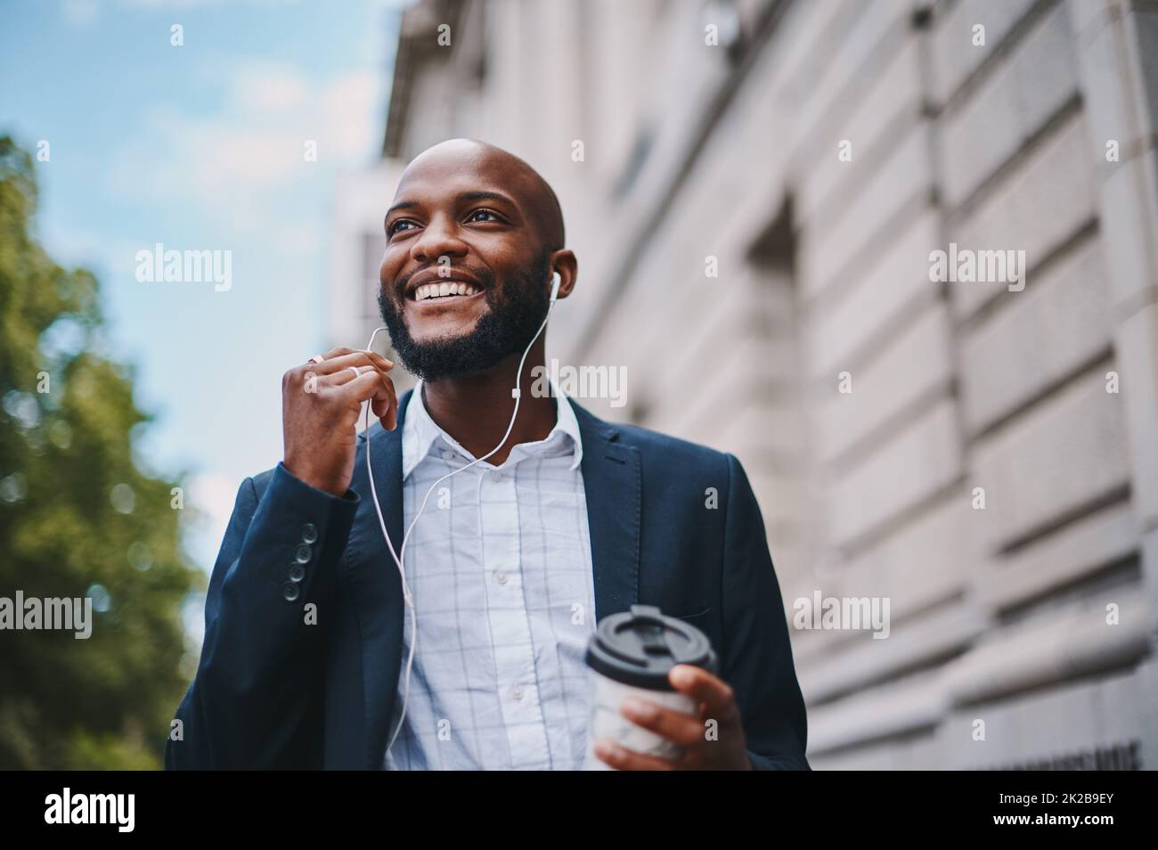 Im che ascolta il mio oratore motivazionale preferito. Immagine di un uomo d'affari che tiene un caffè e ascolta la musica attraverso gli auricolari mentre cammina per la città. Foto Stock