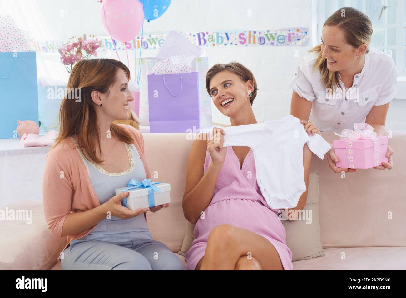 Voi ragazzi state rovinando me - e il bambino. Una giovane donna incinta che riceve regali dai suoi amici graziosi al suo babyshower. Foto Stock