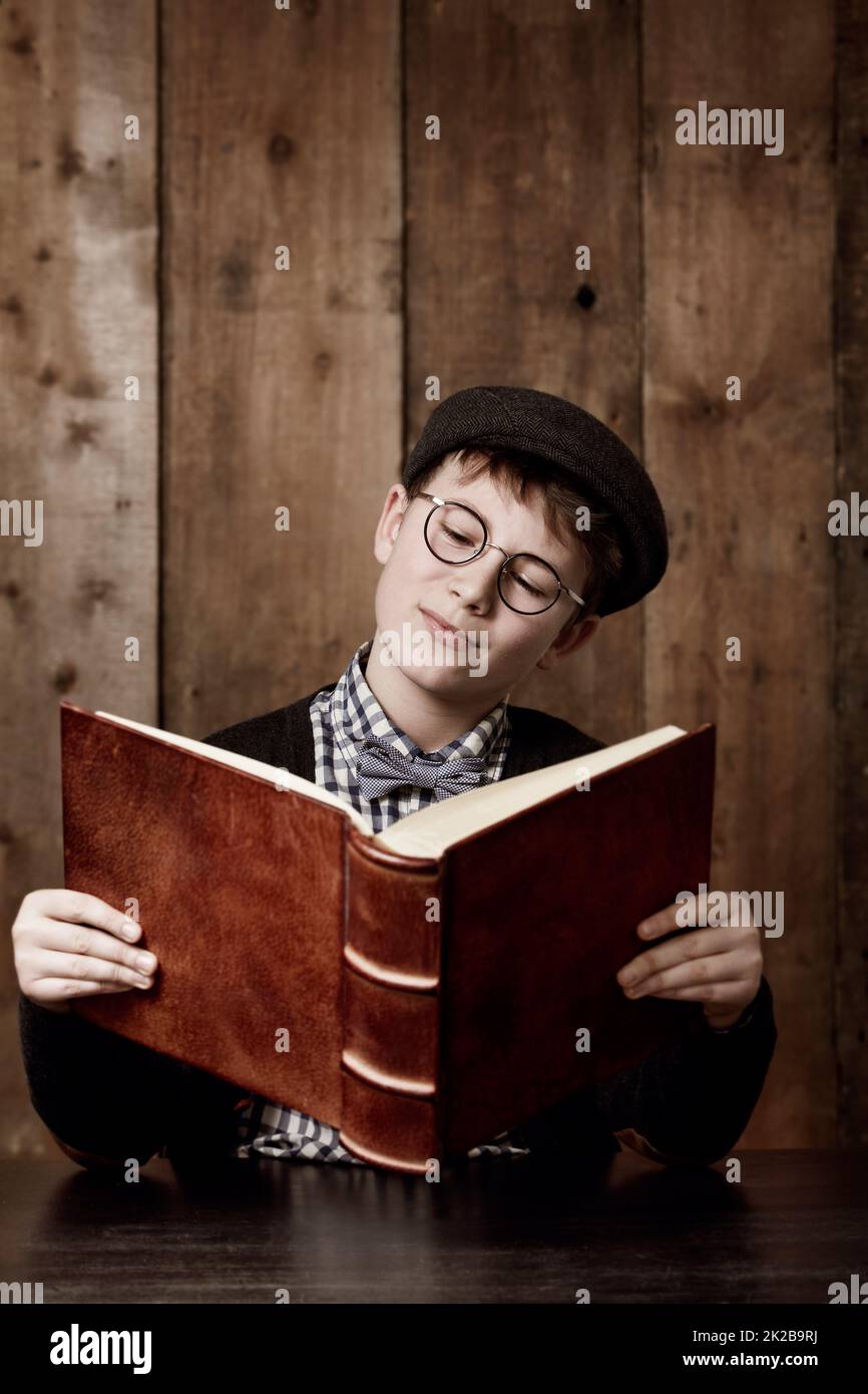 Imparare molte cose nuove. Giovane ragazzo in abbigliamento retrò con occhiali che leggano un libro voluminoso thoughtfully. Foto Stock