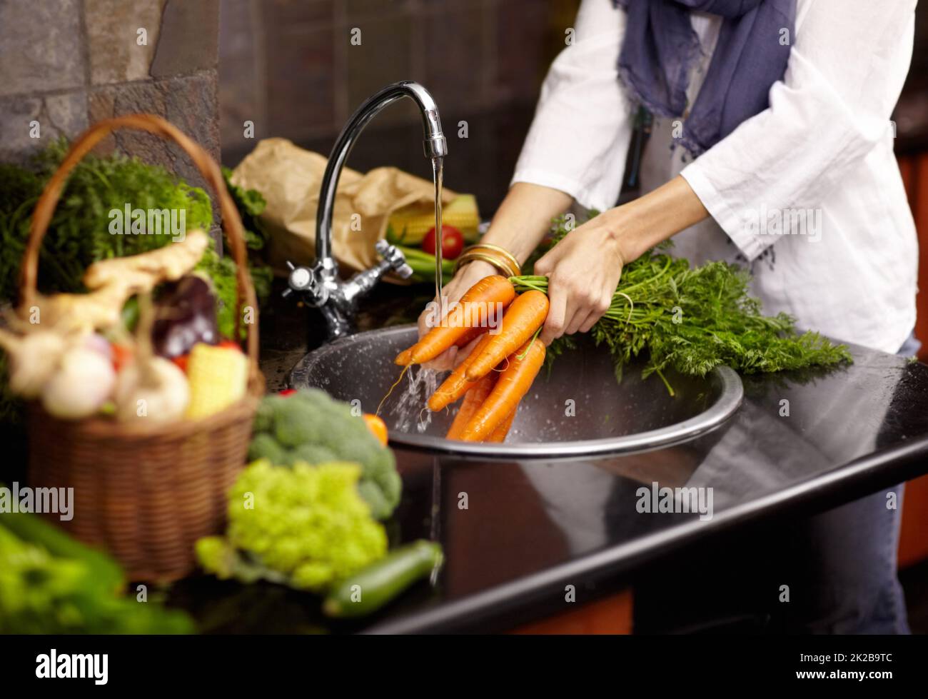 Una donna che usa uno scolapasta e un lavello da cucina per lavare i  pomodori.