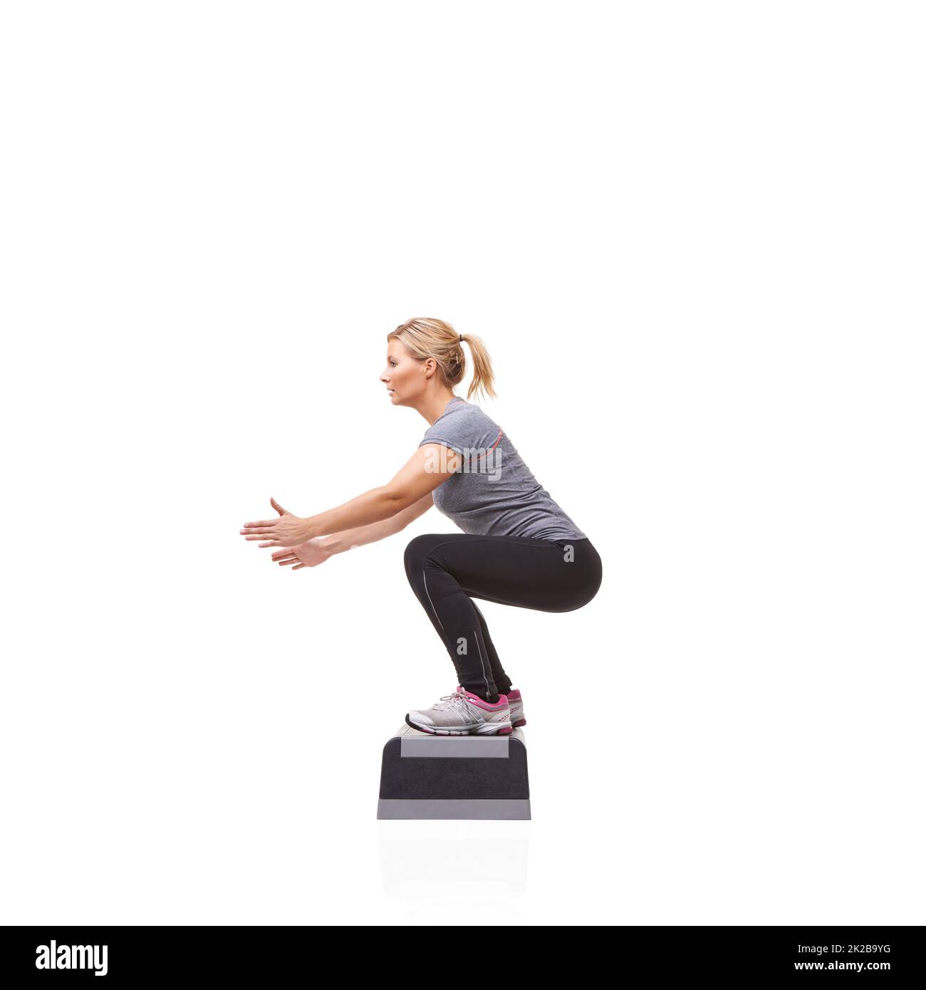 Fare squats per tonificare il suo corpo. Una giovane donna sorridente che fa aerobica su un punto aerobico contro uno sfondo bianco. Foto Stock
