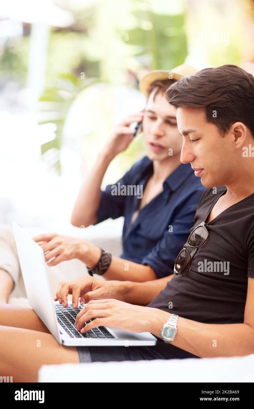 Im controllare i plc mentre parliamo. Un giovane che parla al telefono mentre guarda il suo portatile accanto agli amici. Foto Stock