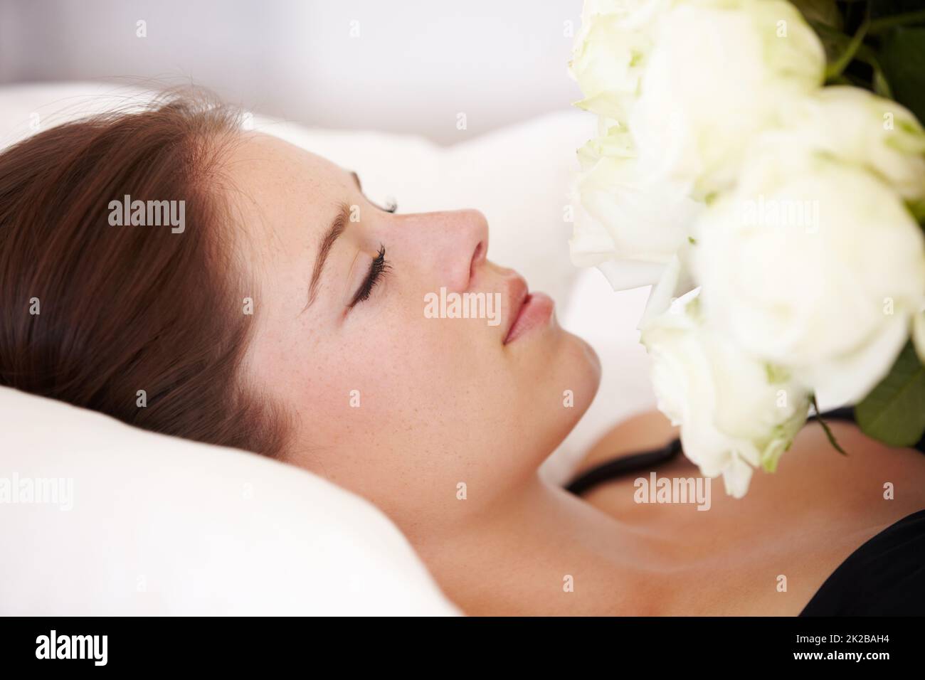Una bellezza del sonno. Una bella giovane donna sdraiata con occhi chiusi e che tiene un bouquet di rose bianche al petto. Foto Stock