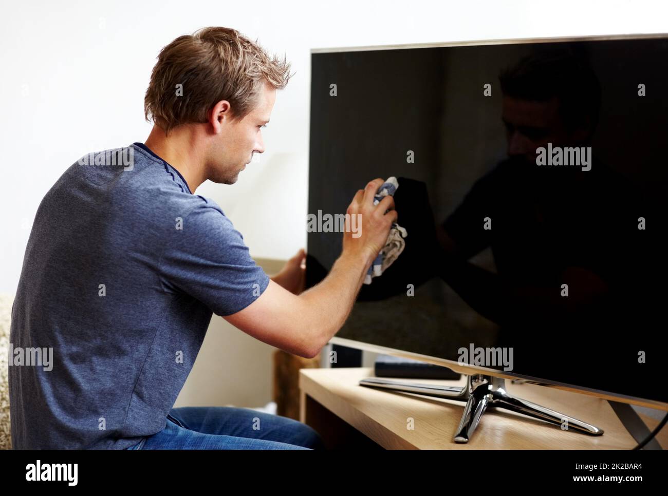 Prendersi cura della sua elettronica. Giovane uomo che pulisce lo schermo della sua Smart TV. Foto Stock