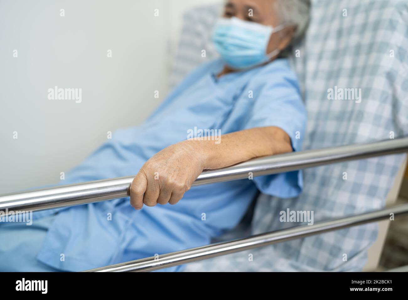 Paziente anziano o anziano asiatico che indossa la maschera per proteggere il coronavirus sdraiarsi maneggiare il letto della rotaia con speranza su un letto in ospedale Foto Stock