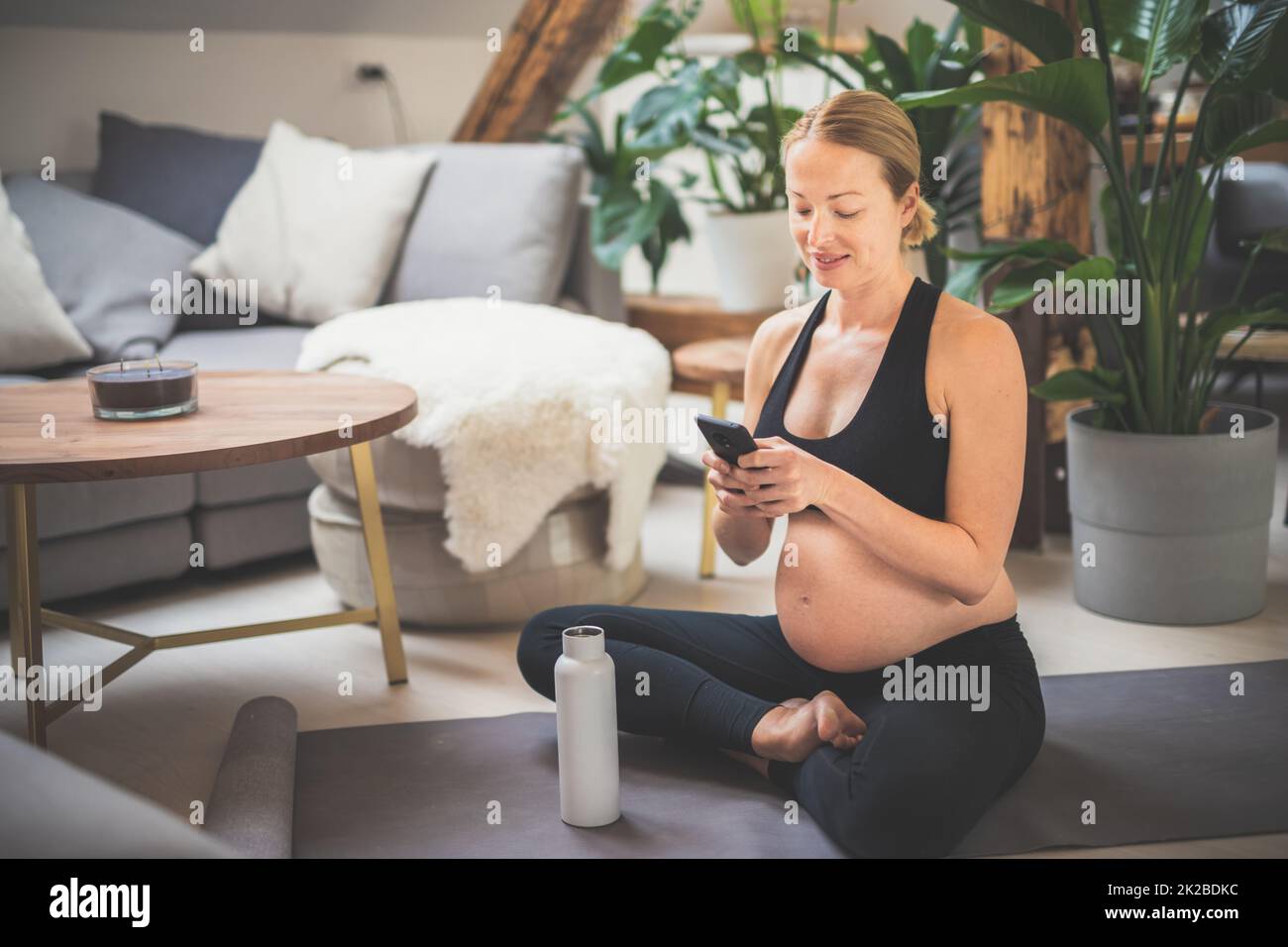 Giovane felice e allegra bella donna incinta chating con la famiglia e gli amici sul telefono cellulare mentre rimanere in forma, sportivo e attivo durante il suo congedo di maternità. Gravidanza, yoga concetto Foto Stock