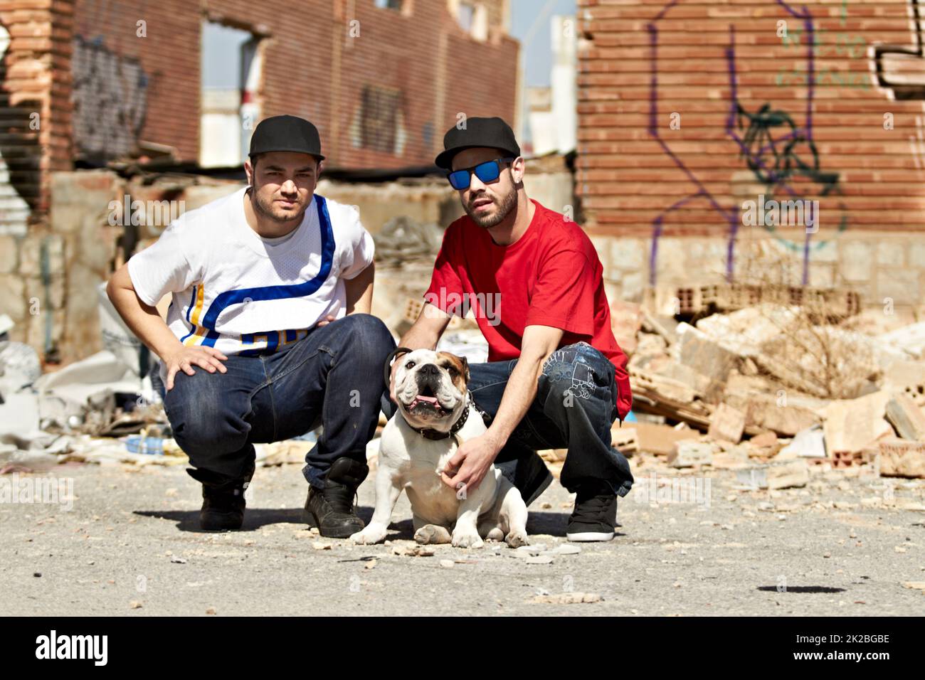 Vivere in un quartiere accidentato. Due maschi urbani inginocchiati con un cane nel loro quartiere. Foto Stock