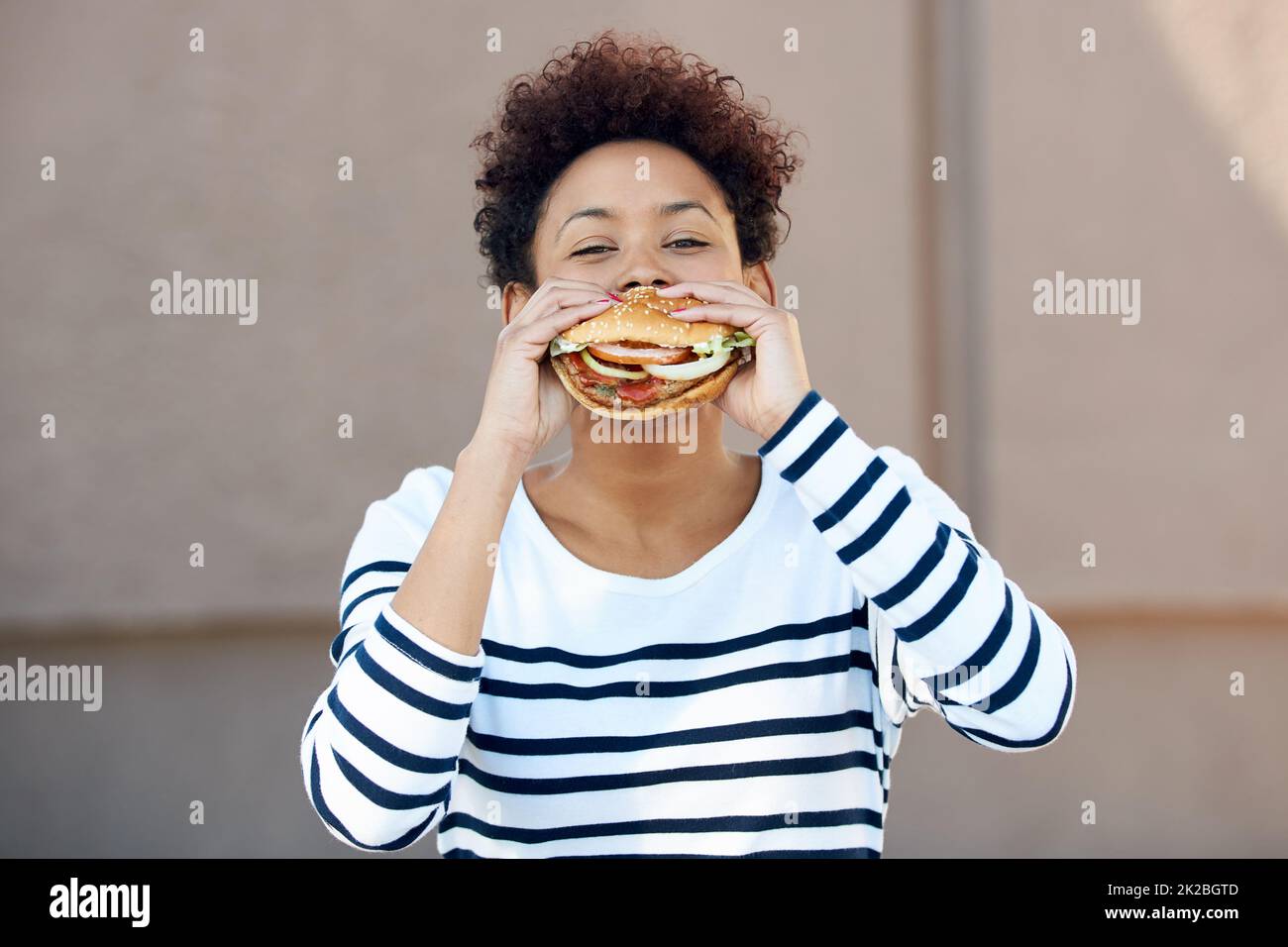 Fast food, se il mio preferito. Ritratto di una giovane donna che mangia un hamburger. Foto Stock