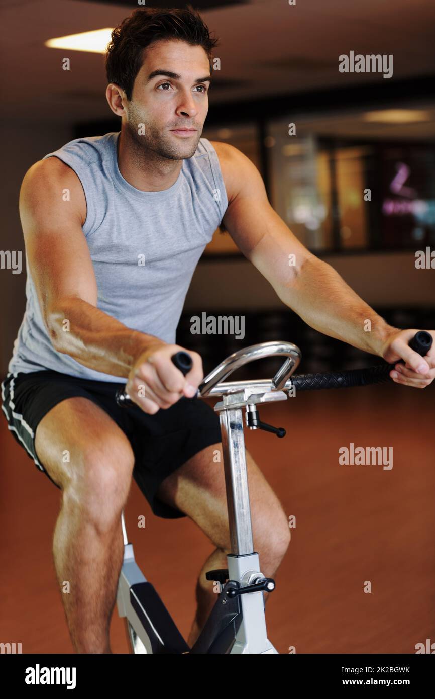 Portando il suo ciclismo a un nuovo livello. Un bel giovane uomo che indossa abbigliamento sportivo e utilizza una bicicletta da ginnastica in palestra. Foto Stock