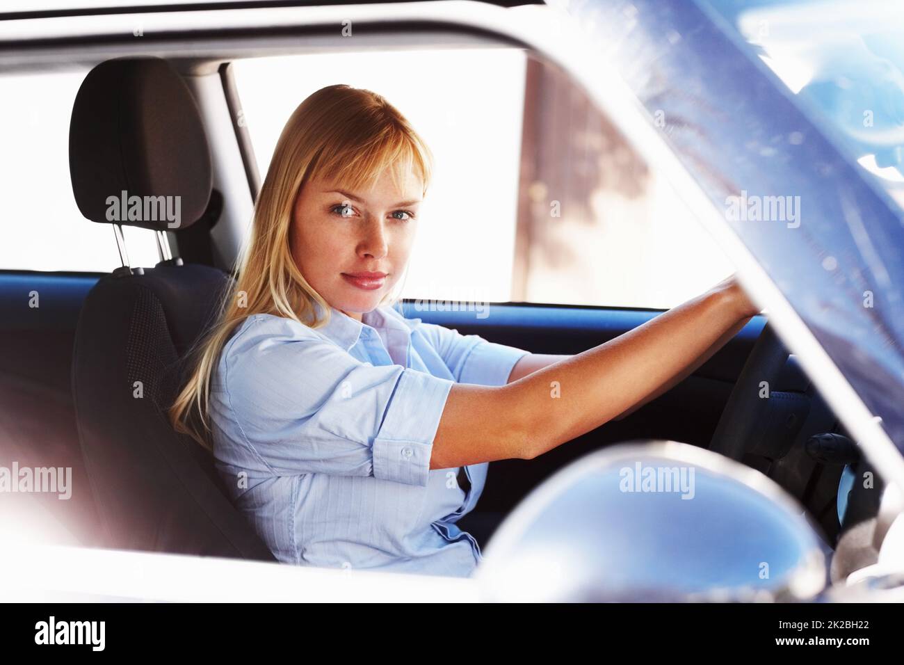 Donna piuttosto giovane al sedile del conducente di una macchina. Bella donna bionda seduta nel sedile del conducente di una macchina. Foto Stock