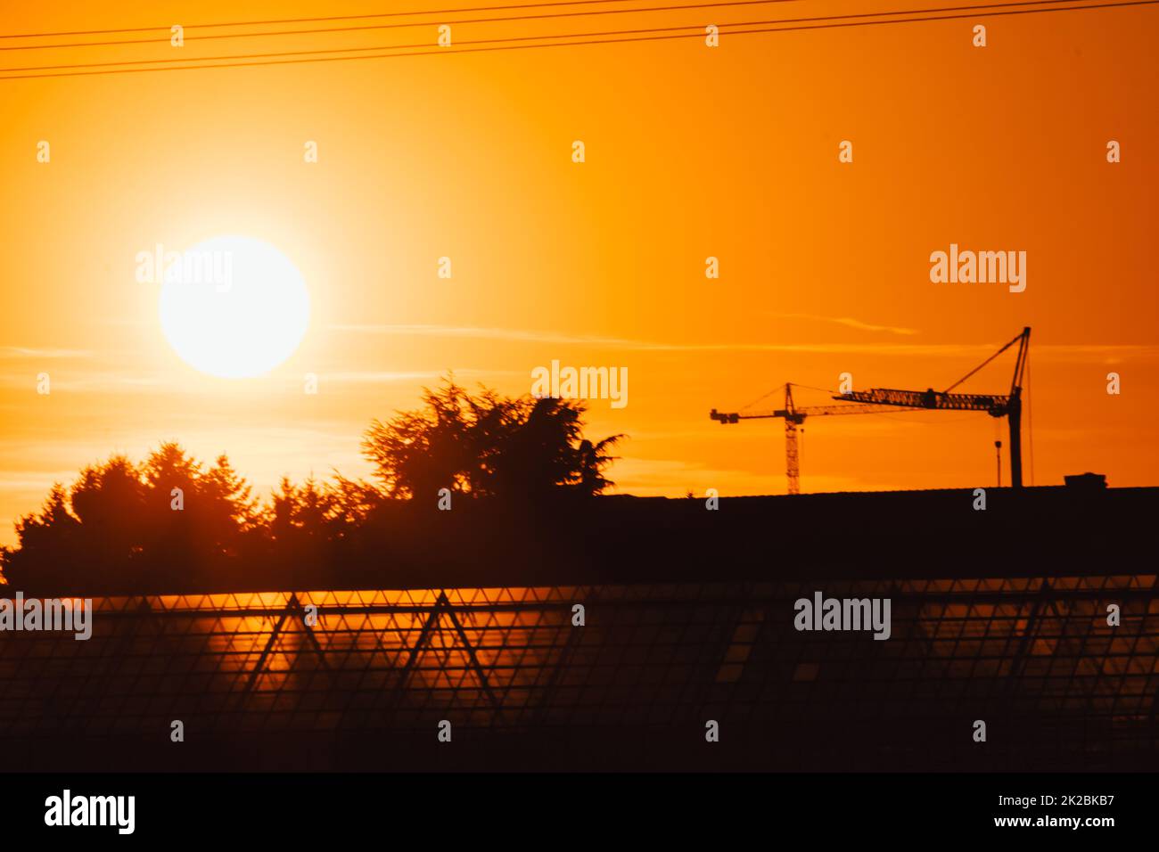 La silhouette di gru da costruzione alta in cielo arancione tramonto mostra il sito di costruzione con l'ingegneria per gli edifici moderni e lo sviluppo della città come lavoro di squadra architettonico per le linee ad alta tensione grattacieli Foto Stock