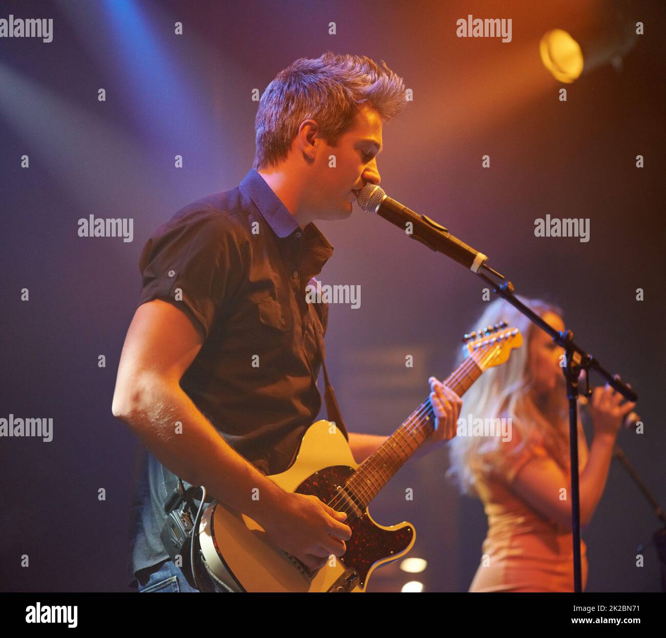 Un frontman espressivo che canta e suona la chitarra ad un concerto. Questo concerto è stato creato per l'unico scopo di questo servizio fotografico, con 300 modelli e 3 band dal vivo. Tutte le persone in questo sparo sono modello rilasciato. Foto Stock