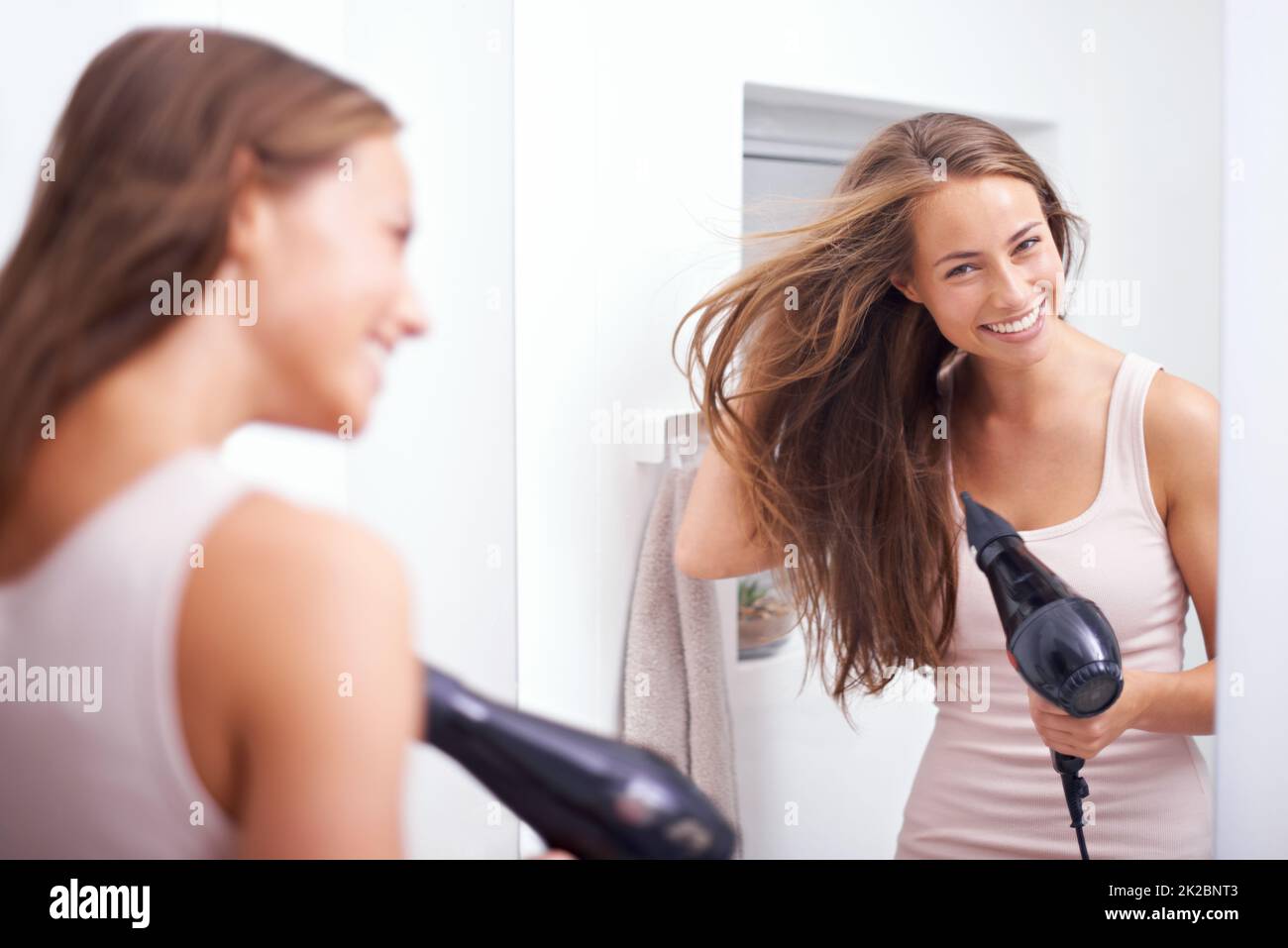 Prendendosi cura della sua mania lusciosa. Una giovane donna soffia asciugando i capelli davanti ad uno specchio. Foto Stock