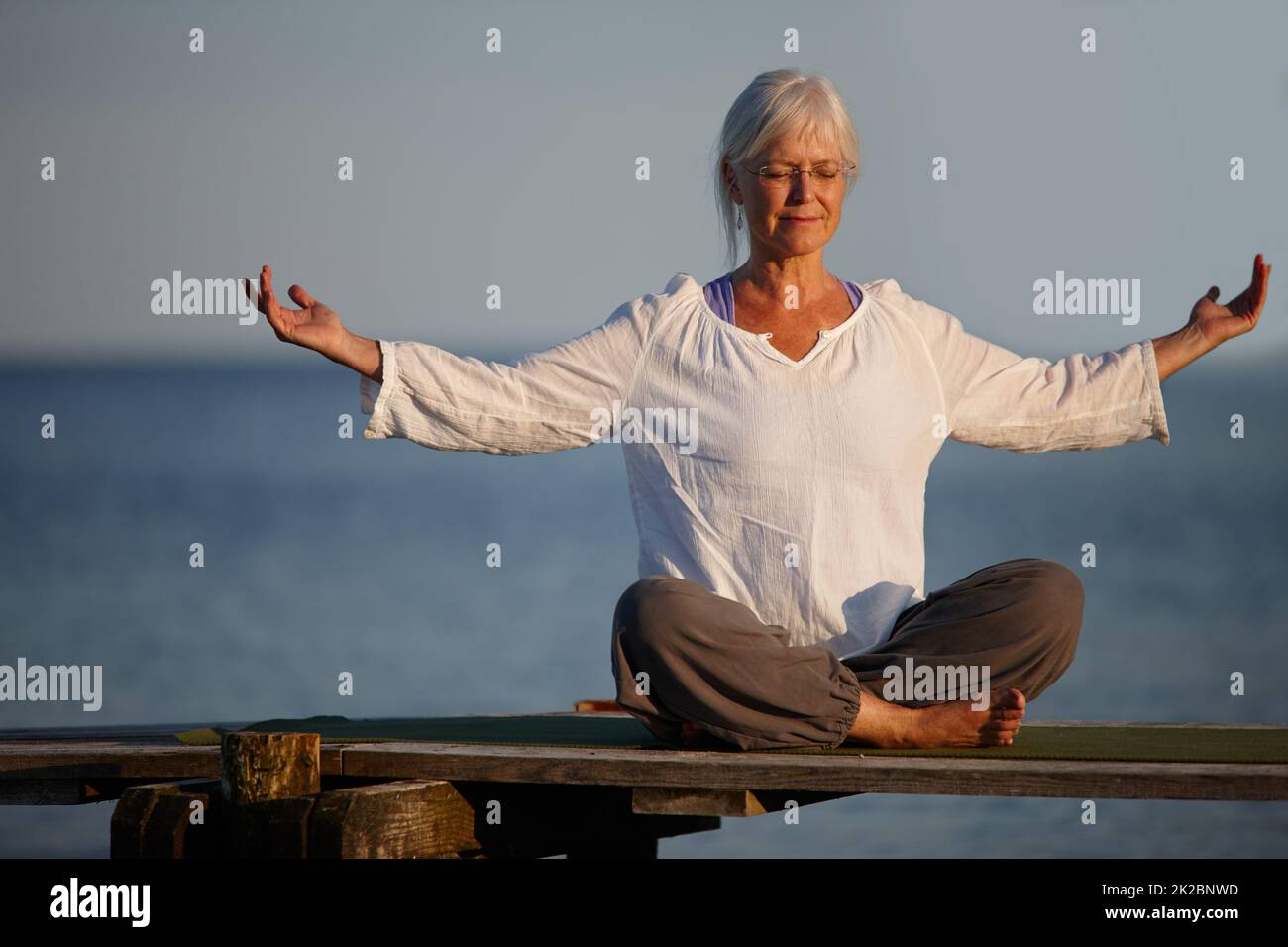 Diventa calmo come l'oceano. Scatto a tutta lunghezza di una donna matura attraente che fa yoga su un molo fuori sull'oceano. Foto Stock