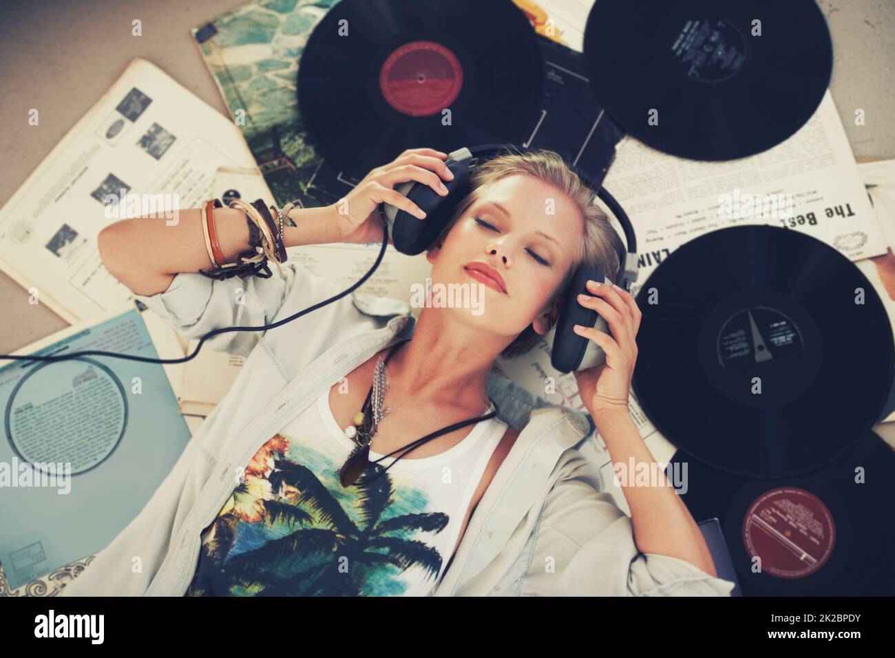 Mantieni la calma e lascia che la musica si riproduda. Una giovane donna che ascolta musica mentre si trova sulla schiena e circondata da dischi. Foto Stock